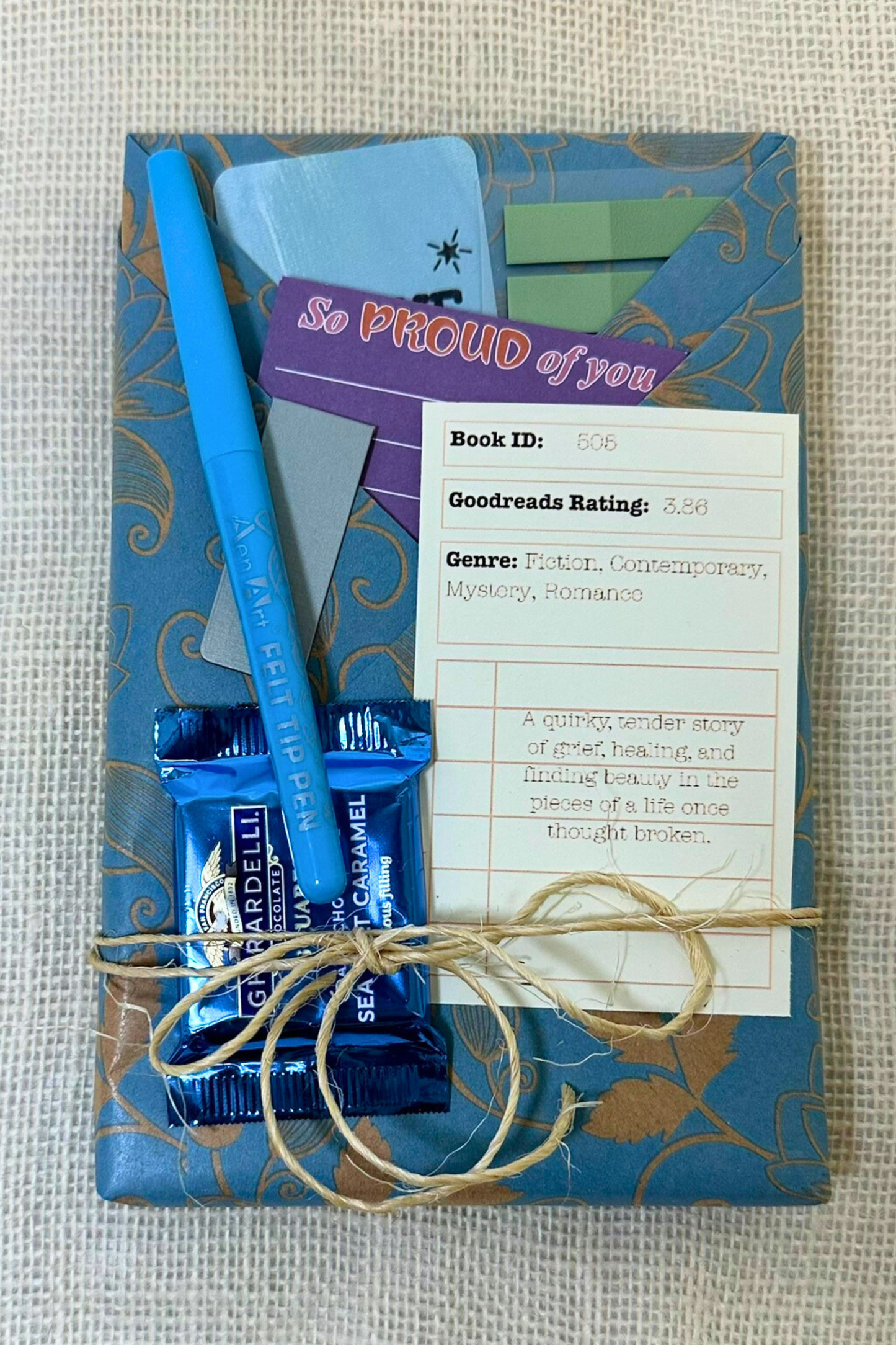 Book wrapped in paper with pockets holding pen, bookmark, sticky notes, and description of the book inside
