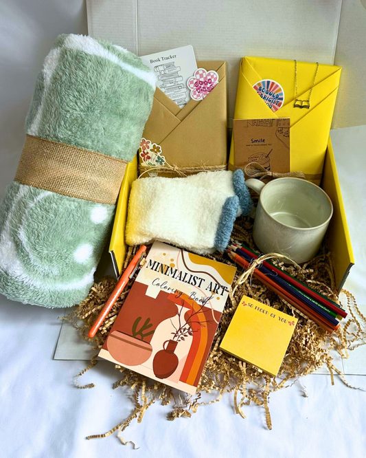 Gift box featuring a blind date with a book along with bookish items including fleece blanket, cozy socks, coloring book, colored pencils, mug, journal, and other bookish items. 