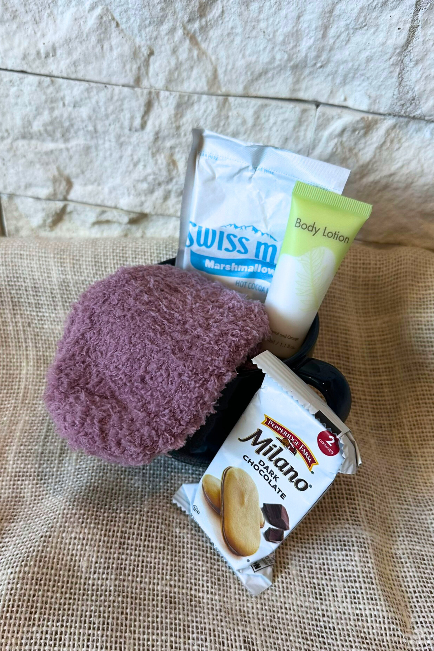Mug with hot chocolate and cozy socks inside. Body lotion and Milano cookies around the mug. 