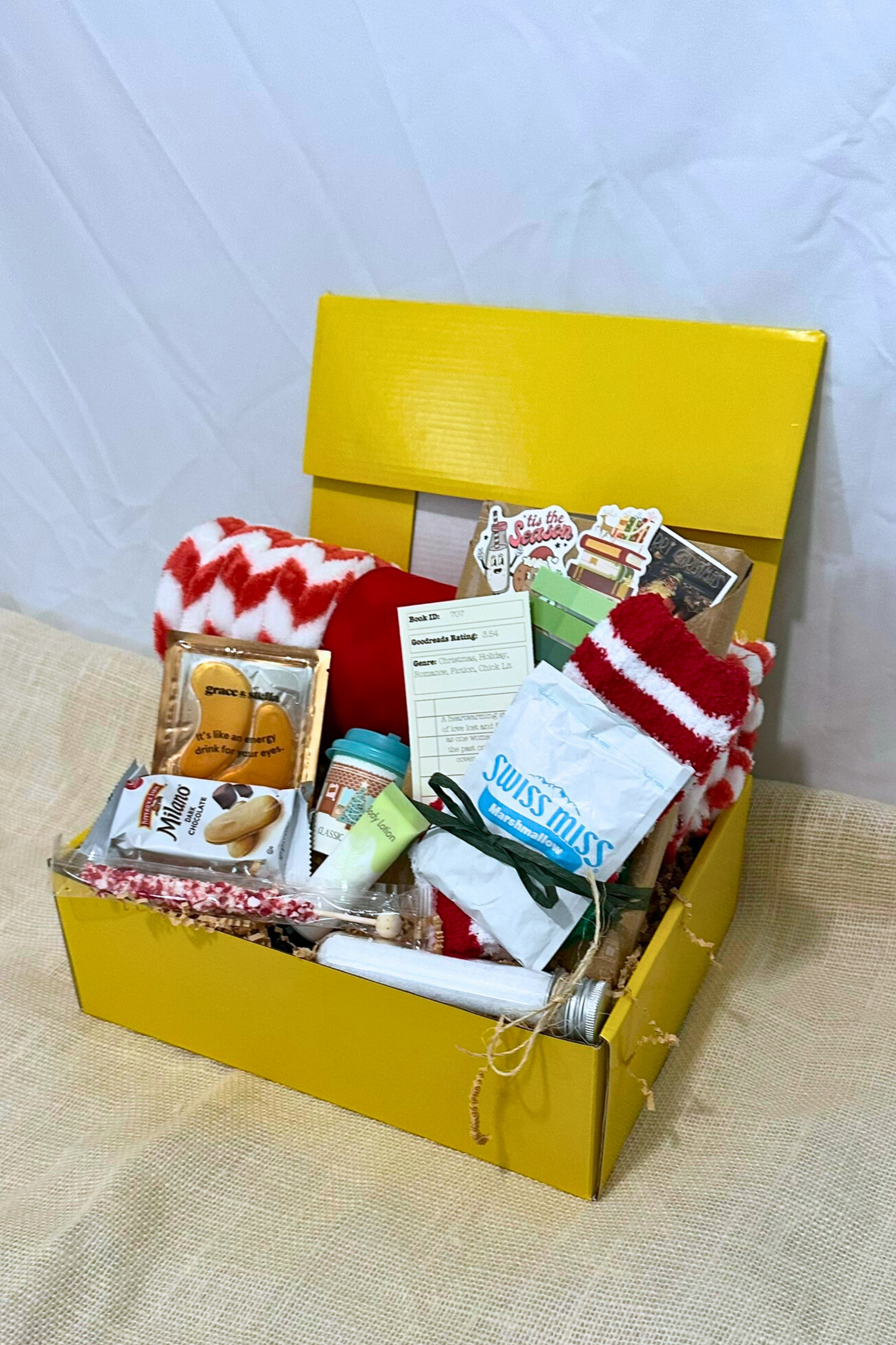 Yellow box filled with winter-themed items including socks, snacks, bath salts, fleece blanket, and blind date with a book