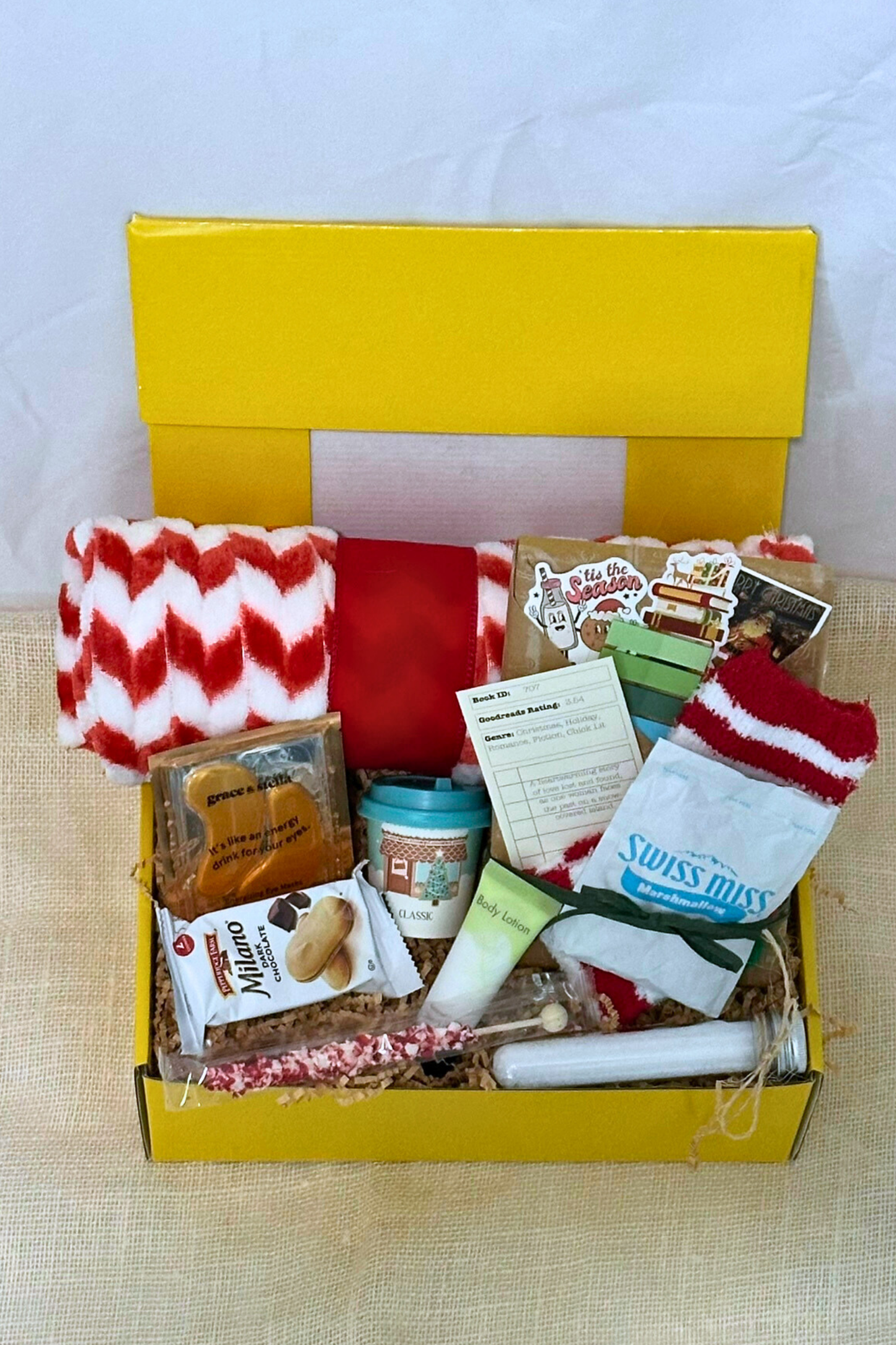 Yellow box filled with winter-themed items including socks, snacks, bath salts, fleece blanket, and blind date with a book