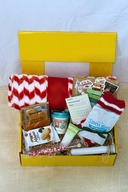 Yellow box filled with winter-themed items including socks, snacks, bath salts, fleece blanket, and blind date with a book