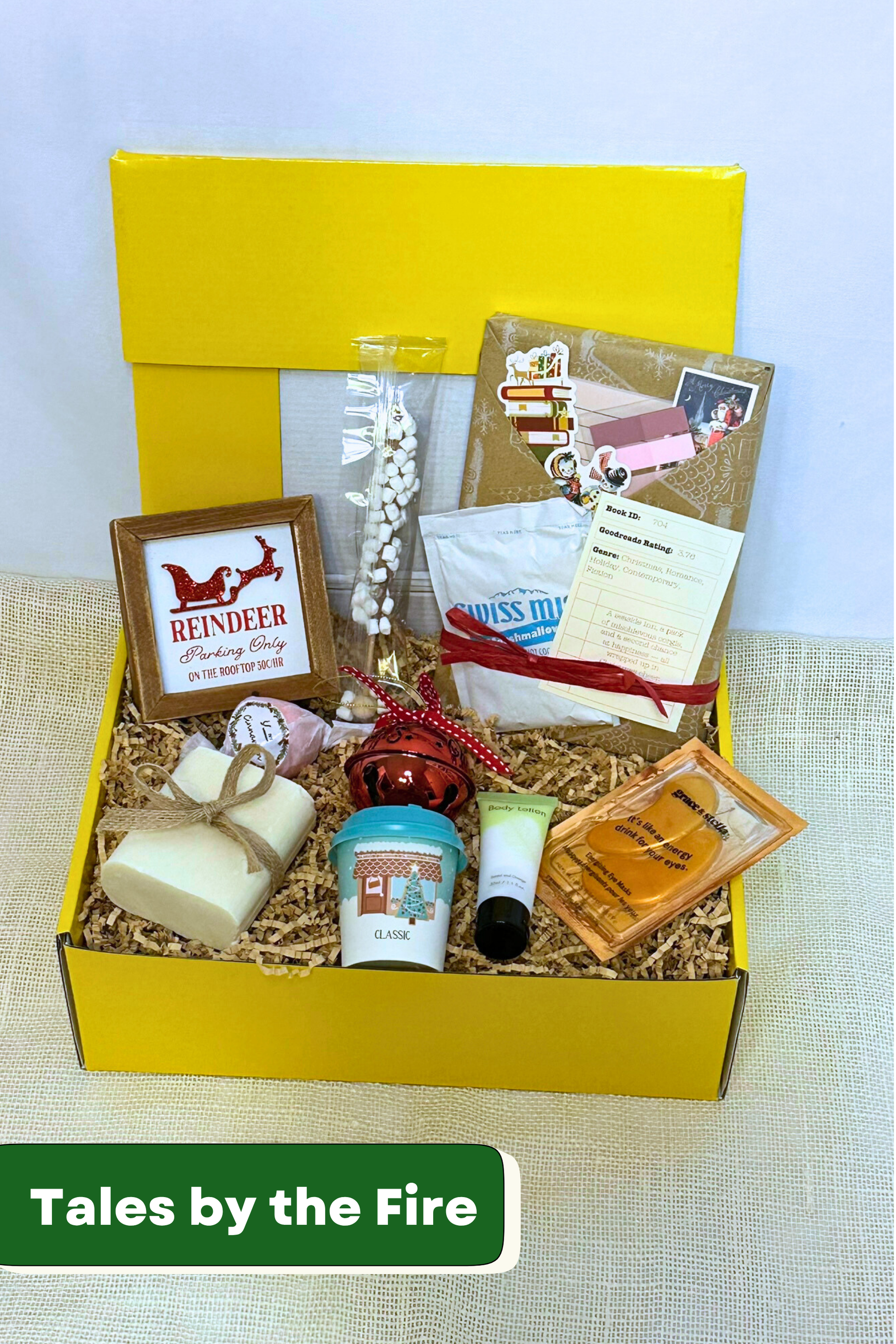 Gift box with various holiday items including handmade bar soap, body lotion, holiday decorations, hot chocolate, and blind date with a book.