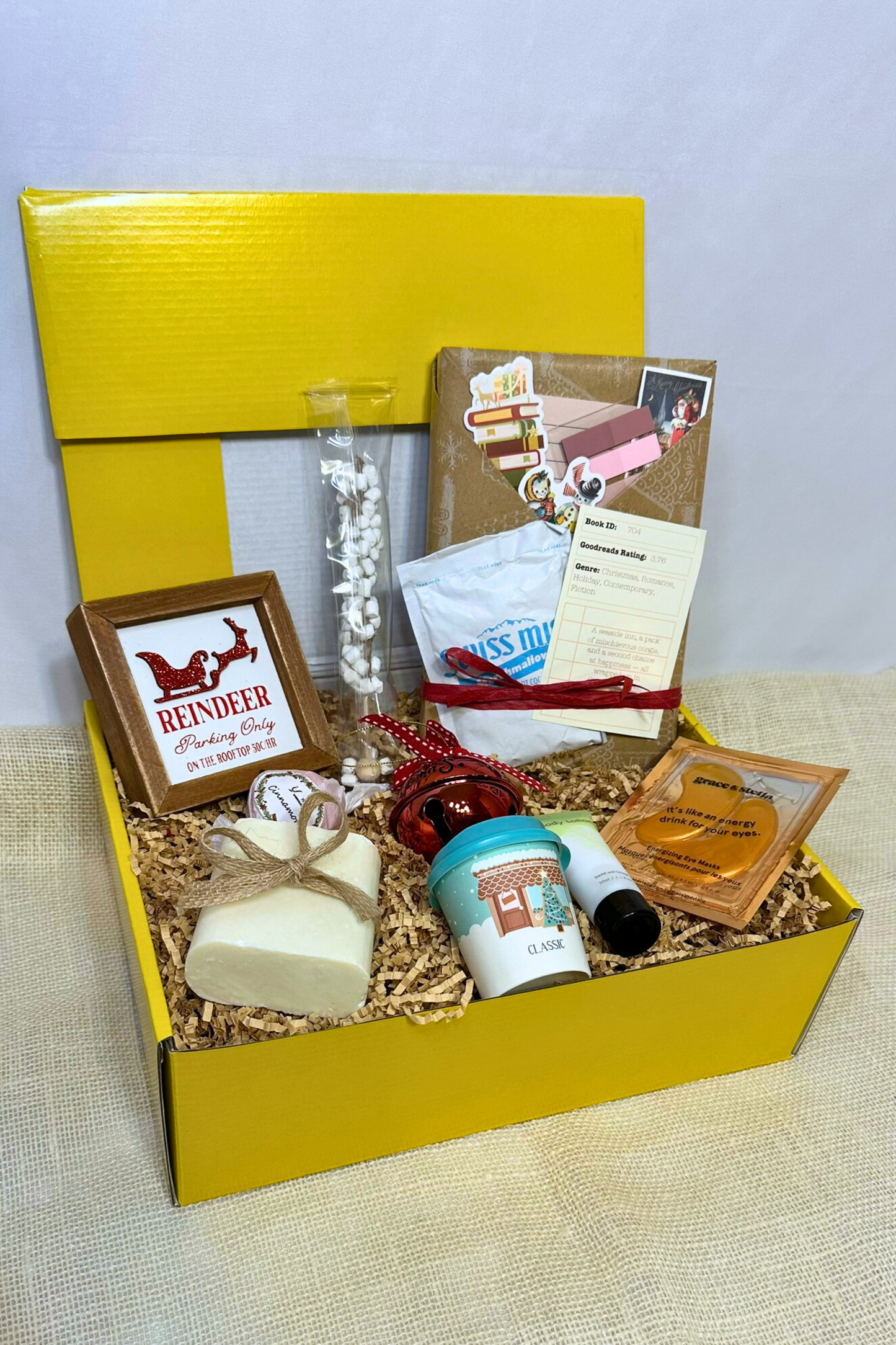 Gift box with various holiday items including handmade bar soap, body lotion, holiday decorations, hot chocolate, and blind date with a book.