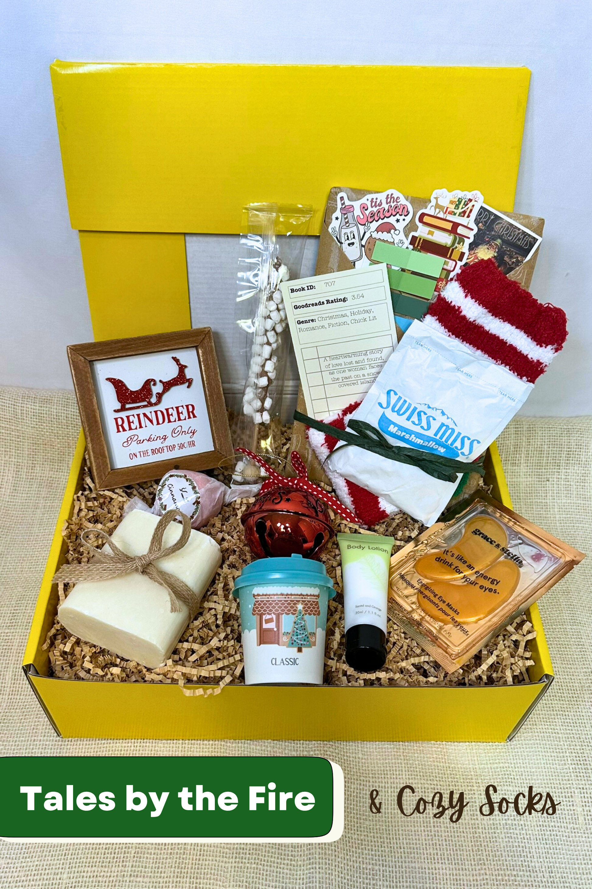 Gift box with various holiday items including handmade bar soap, body lotion, holiday decorations, hot chocolate, cozy socks, and blind date with a book.