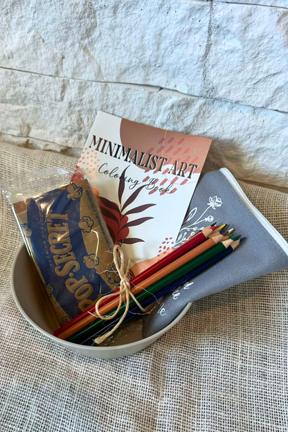 Popcorn bowl with popcorn, adult coloring book, colored pencils, and zipper pouch inside the bowl. 