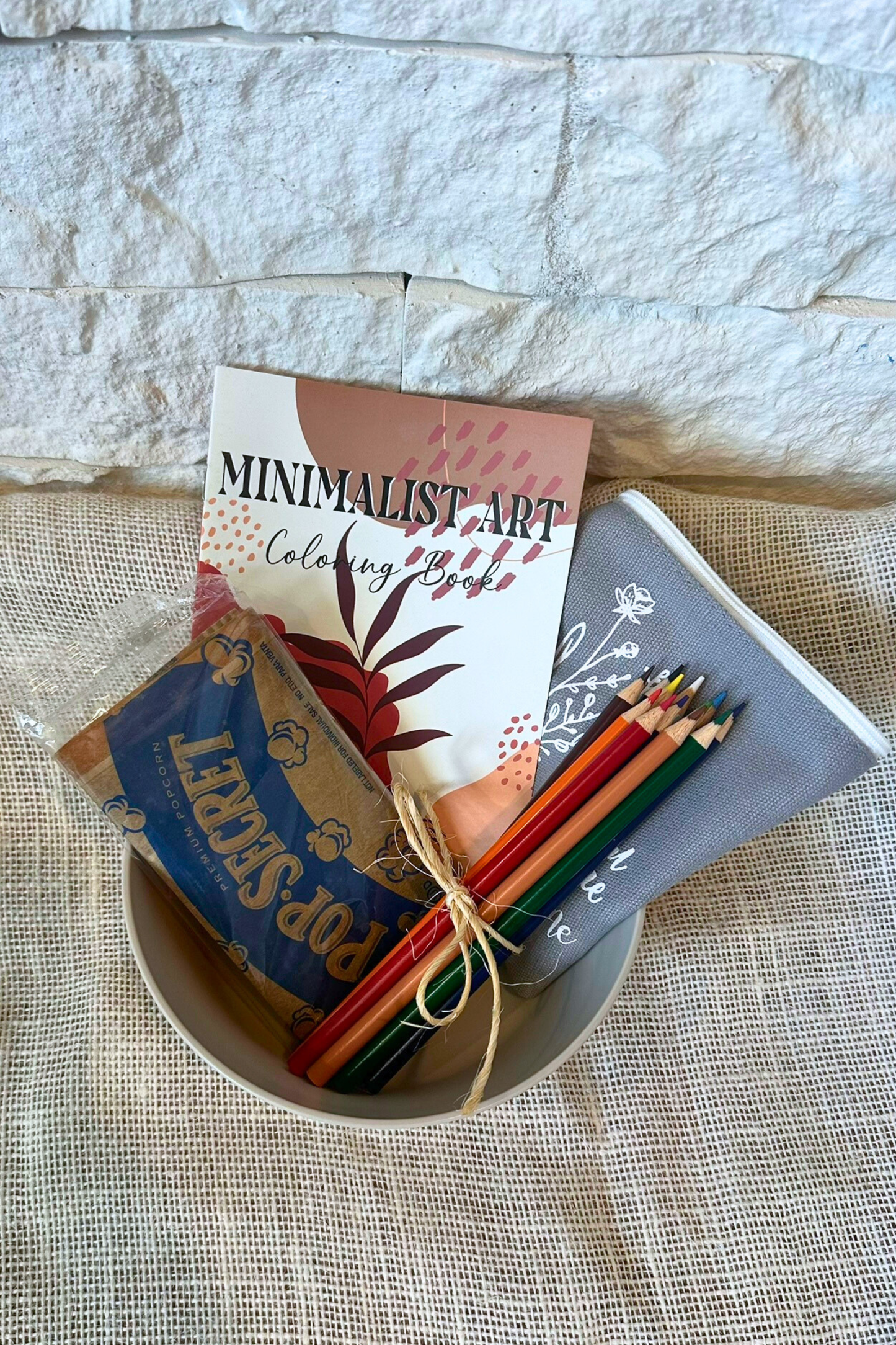 Popcorn bowl with popcorn, adult coloring book, colored pencils, and zipper pouch inside the bowl. 