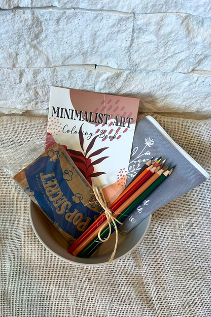 Popcorn bowl with popcorn, adult coloring book, colored pencils, and zipper pouch inside the bowl. 