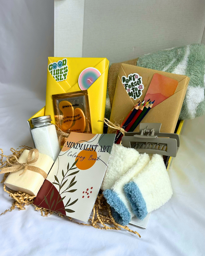 Gift Box with fleece blanket, cozy socks, bar soap, bath salts, coloring book, colored pencils, hair clip, featuring a blind date with a book with bookish items. 